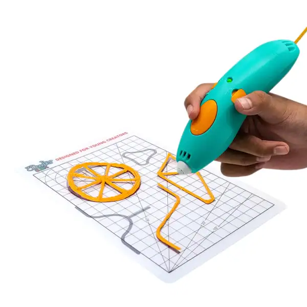 A hand uses a teal and orange 3D printing pen to draw shapes with yellow filament on a gridded template sheet, including a wheel and a triangle.