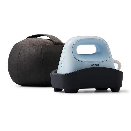 A compact Cricut heat press with a light blue handle sits in a black base, next to a round, dark gray pressing cushion.