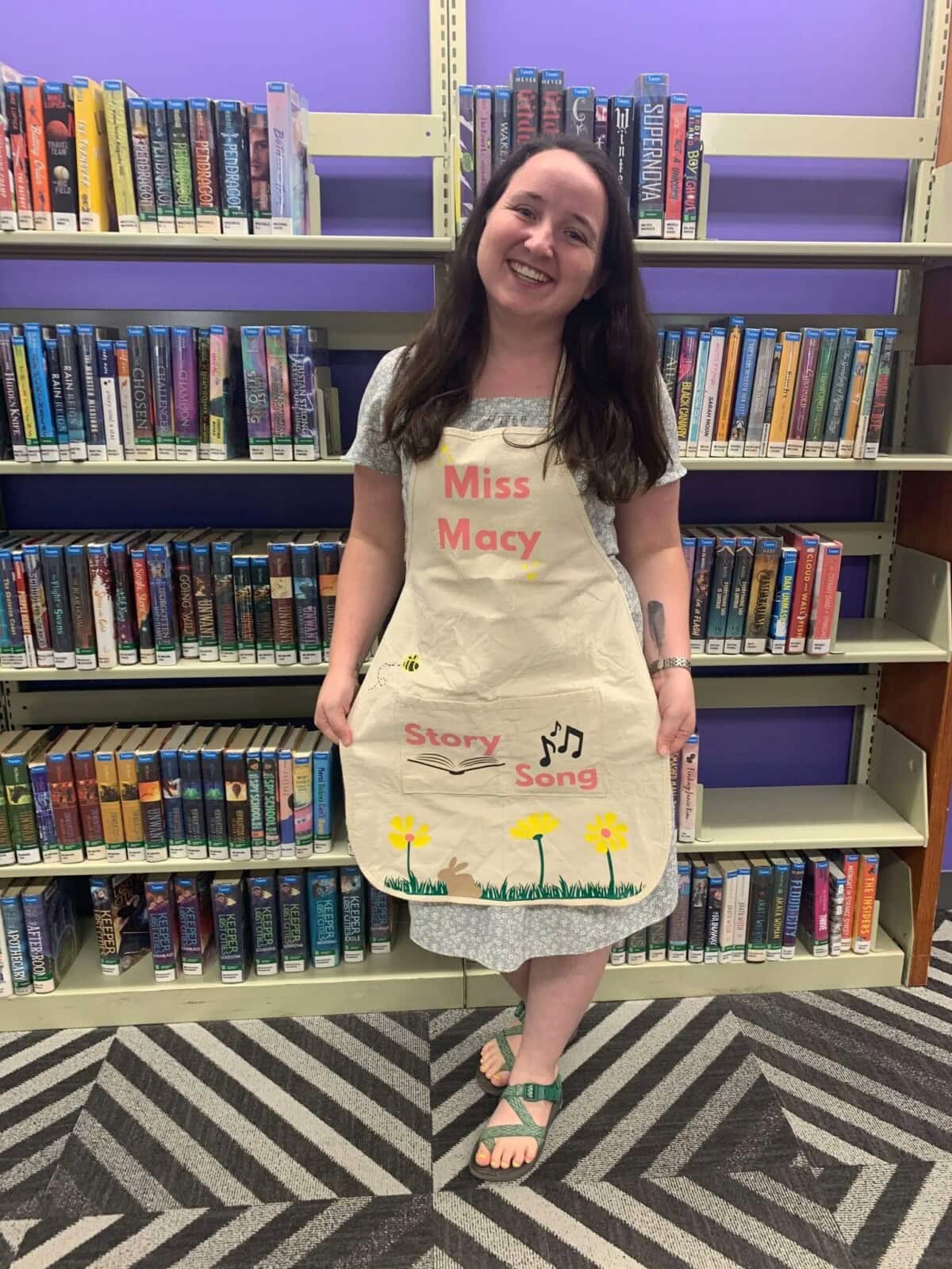 A smiling woman wearing an apron that says Miss Macy.